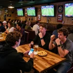 Fan placing bets on keobongda app while watching live sports in a vibrant bar atmosphere